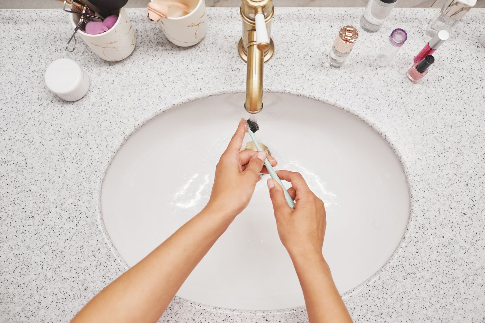 Hands rinsing a toothbrush under running water in a bright bathroom