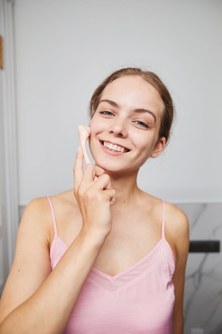 A Smiling Woman Using A Facial Massager