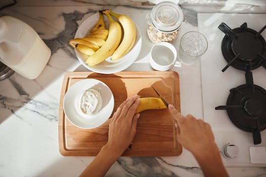 Person slicing banana on wooden board with cereals and milk for a healthy breakfast.