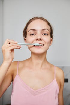 Woman in pink pajamas practicing oral hygiene with a toothbrush indoors.