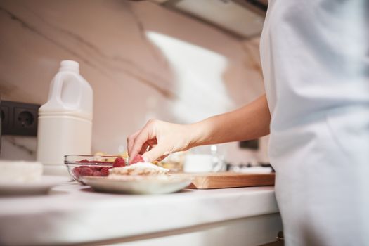 A close-up of a person preparing a raspberry dish on a kitchen counter.