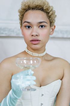Elegant portrait of a young woman in period costume holding a cocktail glass, set indoors.
