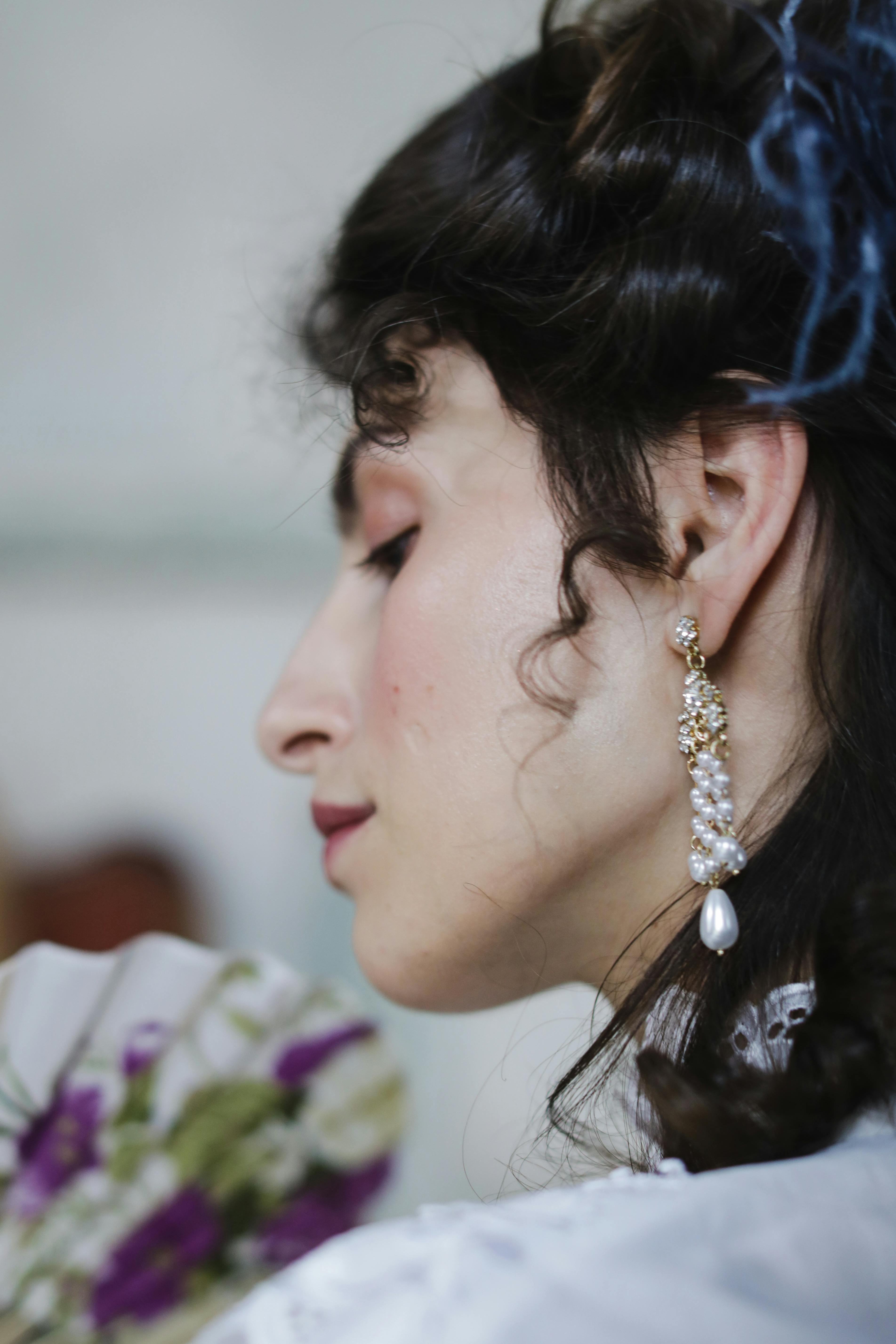 Close-up of a woman wearing a pearl earring and holding a floral hand fan.