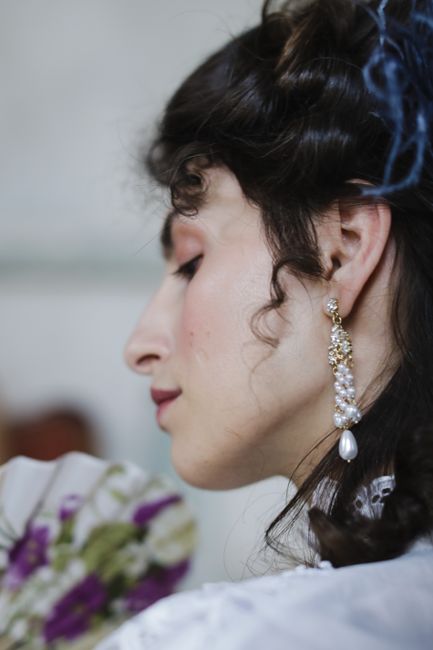 Close-up of a woman wearing a pearl earring and holding a floral hand fan.