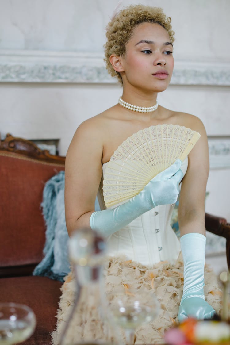 A Woman Wearing Tube Dress Sitting On A Couch While Holding A Hand Fan