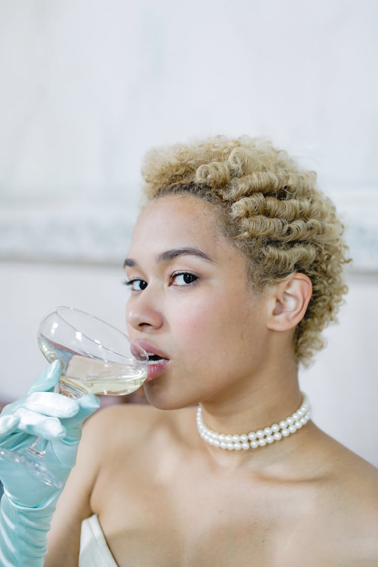 A Woman Wearing A Pearl Necklace Drinking Wine