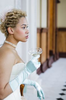 A stylish woman with curly hair and gloves, holding champagne in an elegant setting.