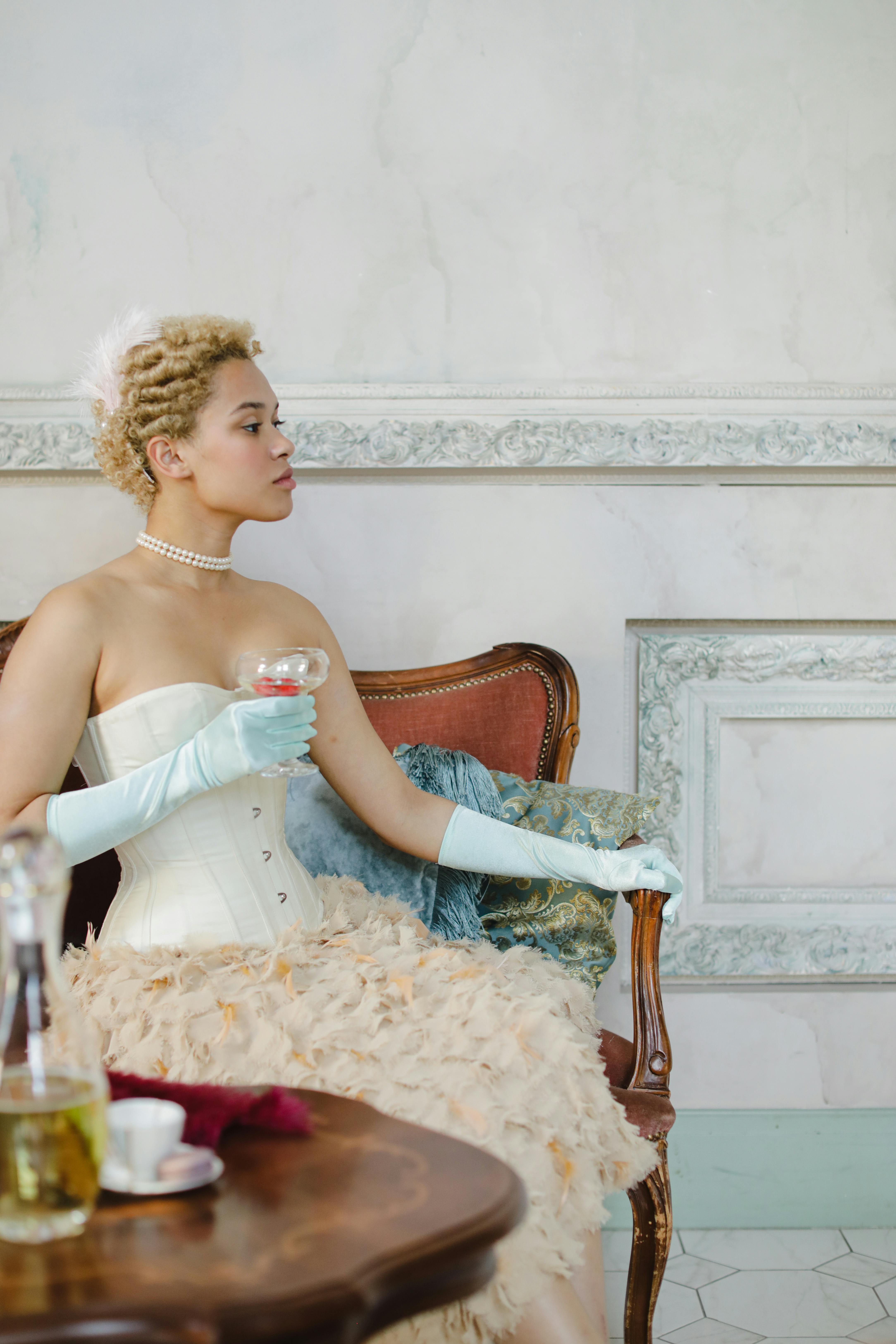 Stylish woman in a vintage corset and gloves holding a wine glass indoors.