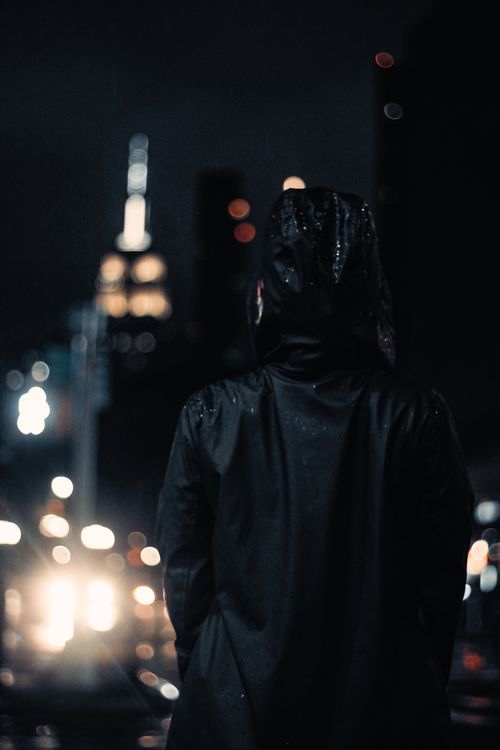 Free A person stands in a black jacket at night, with city lights and bokeh in the background. Stock Photo