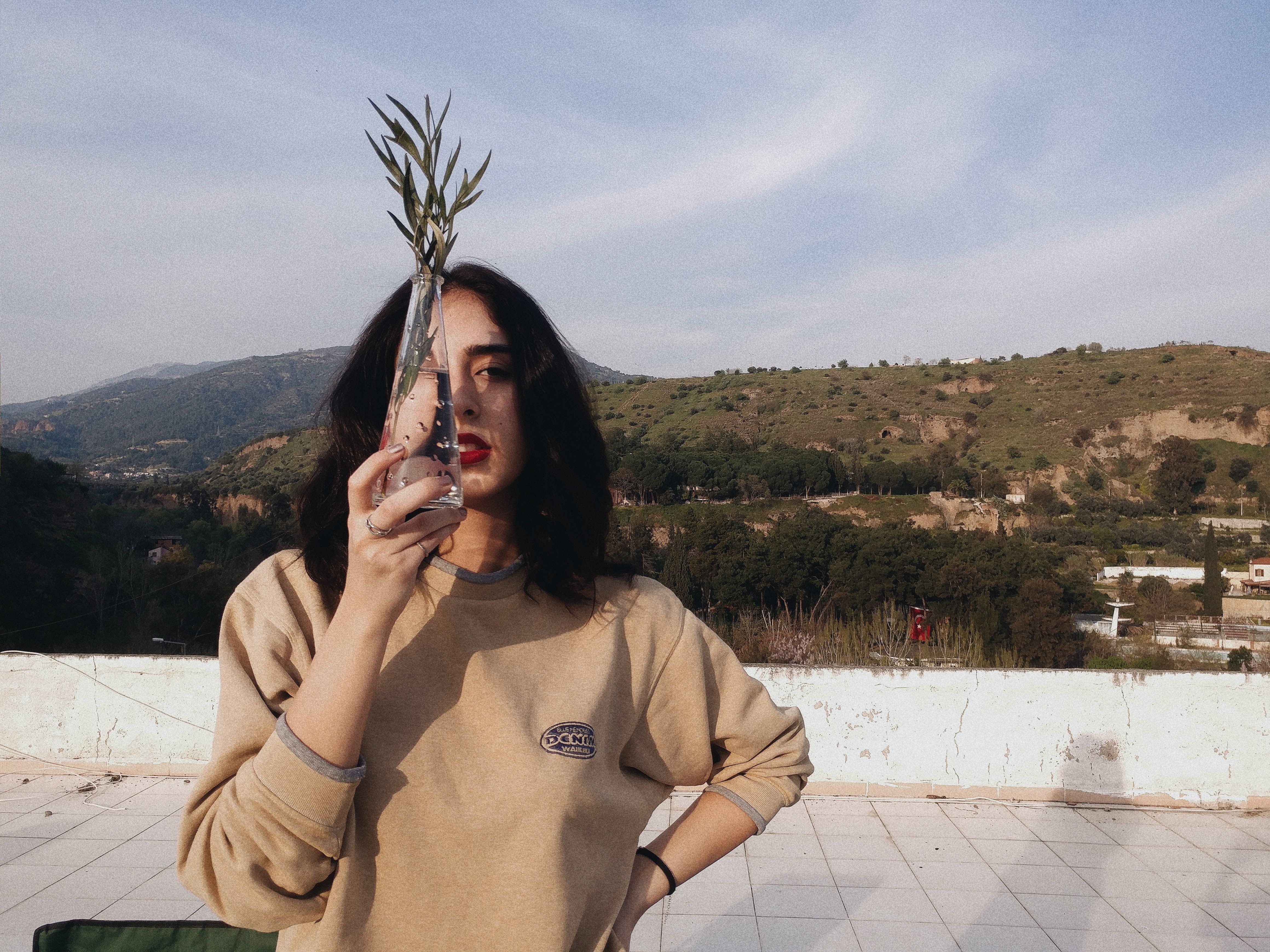 Stylish woman on a rooftop holding a glass vase, enjoying a sunny day outdoors.