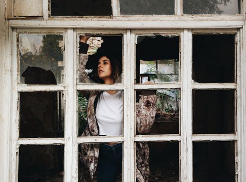 Free A woman in a stylish pose framed by a broken window in an abandoned building. Stock Photo