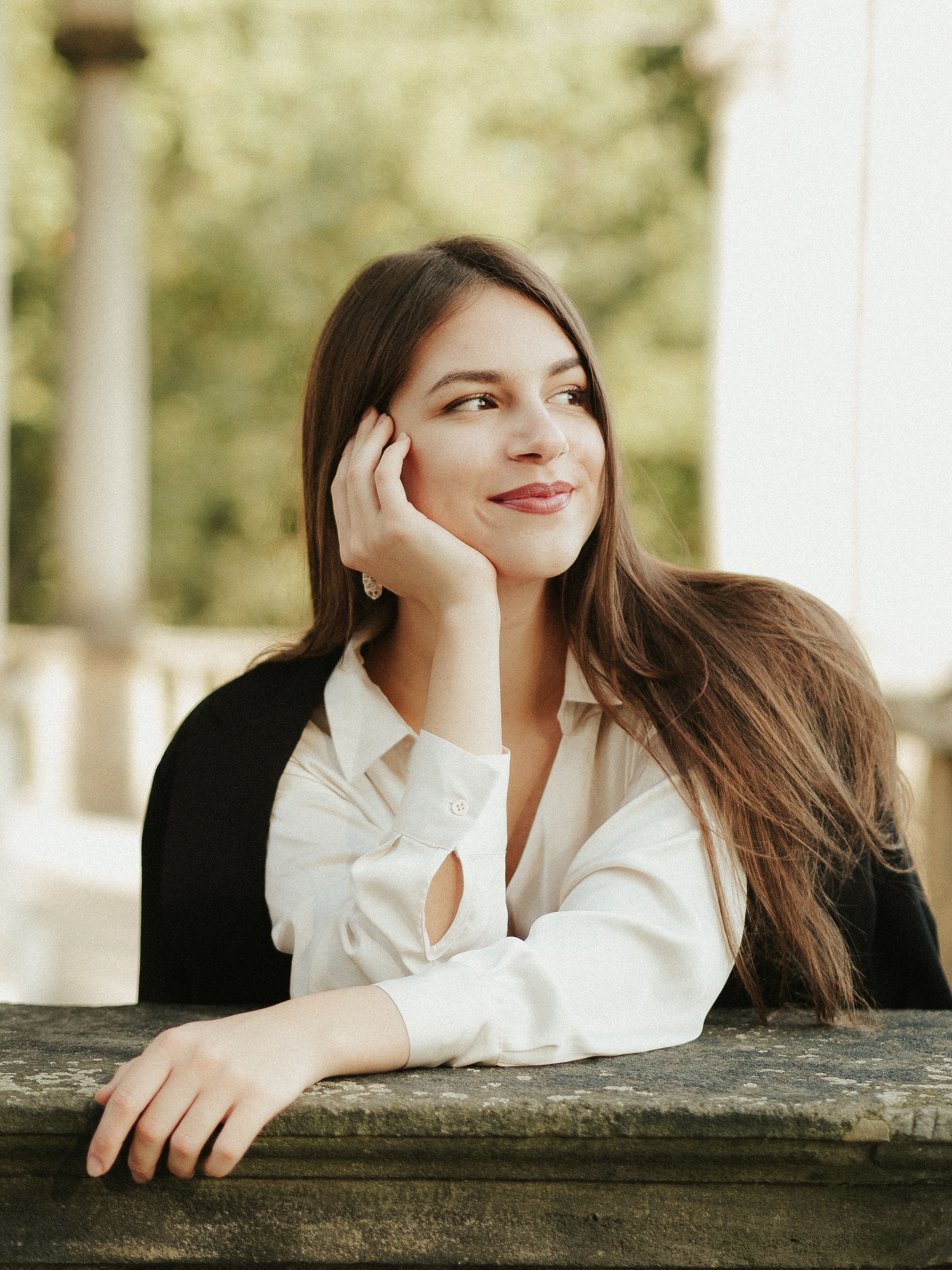 Young woman in a white blouse smiling outdoors, exuding elegance and warmth.