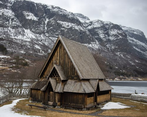 Brown Wooden House Near the Lake and Snow Covered Mountains