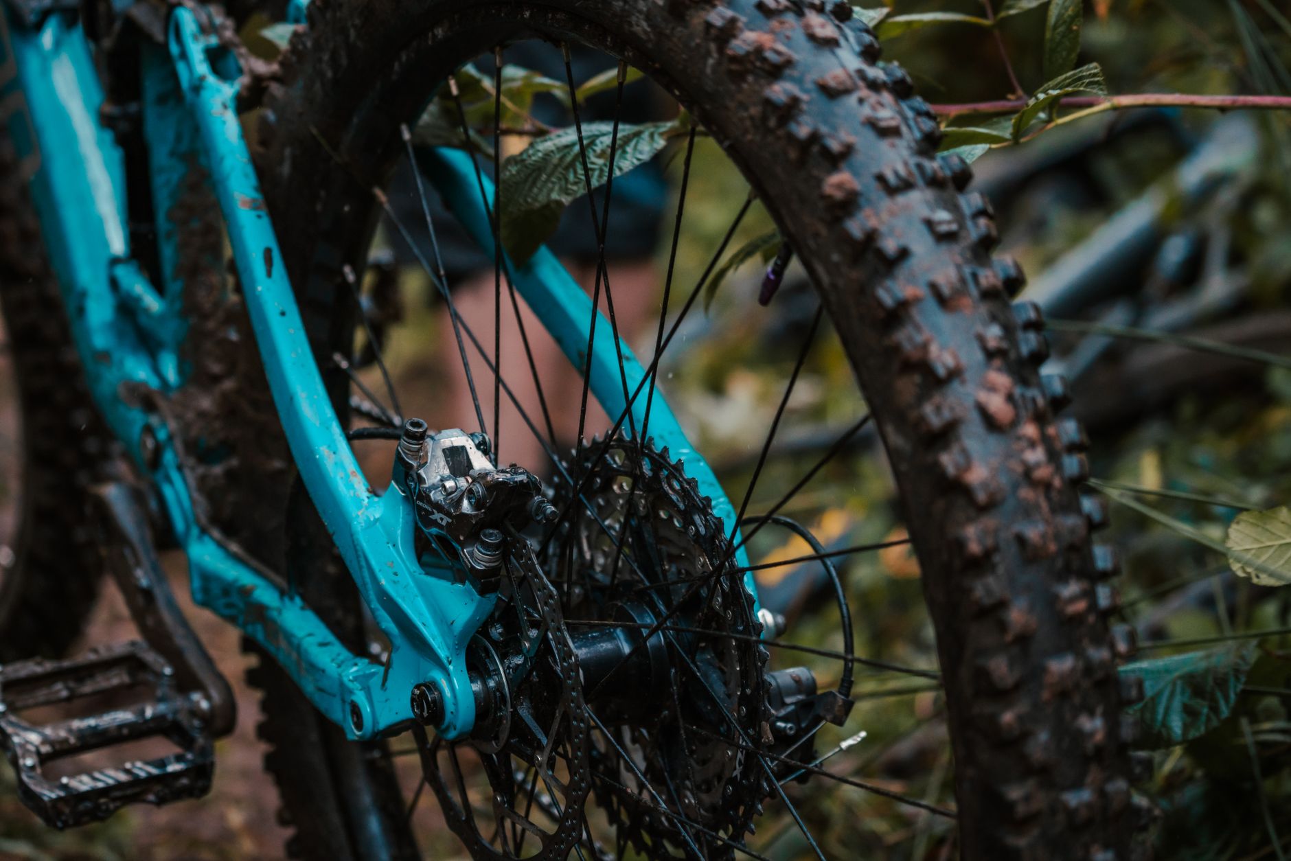 Rear end of a muddy full-suspension trail bike, Shimano XT cassette, caliper, and hub in focus.