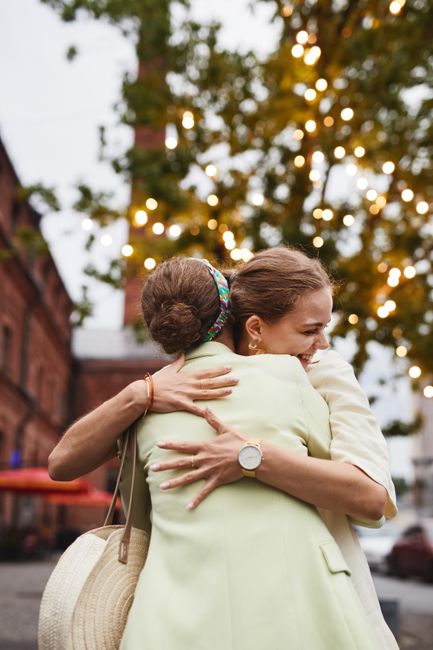 Fotomural Dos mujeres adultas se abrazan con alegría al aire libre con luces de fondo, transmitiendo amistad y felicidad.