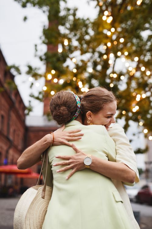 Free Two adult women joyfully hug outdoors with lights in the background, conveying friendship and happiness. Stock Photo