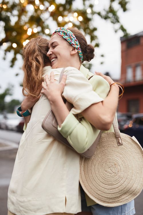Free Two women sharing a joyful embrace on a vibrant street setting. Stock Photo