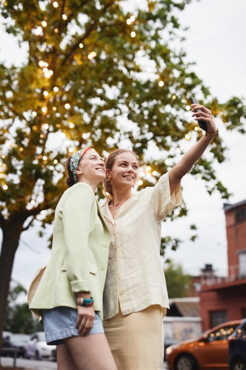 Free Joyful friends capturing a fun moment with a selfie under a tree with lights. Stock Photo