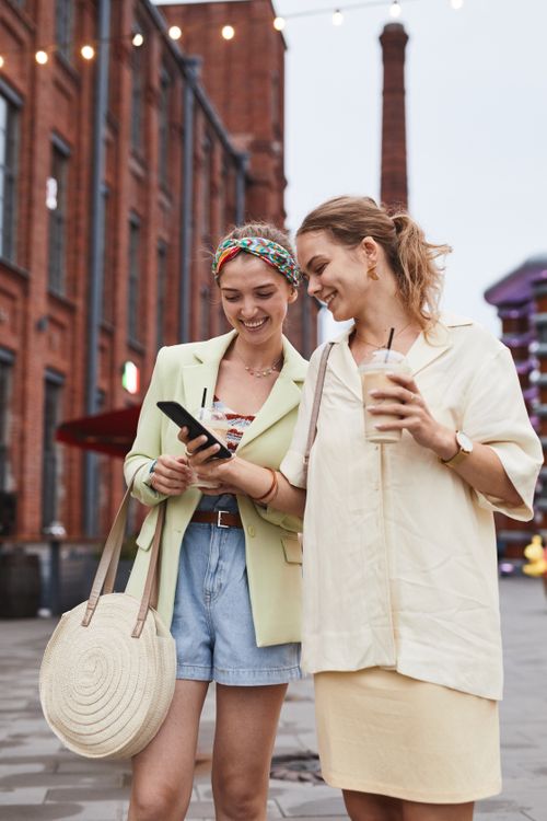 Free Two fashionable women walking outdoors, smiling and enjoying each other's company. Stock Photo