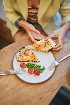 Top view of person with smoked salmon bagel on plate with peas and tomatoes.