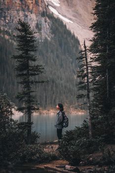 A woman stands in Banff National Park, Canada, admiring the scenic lake view surrounded by trees.
