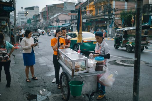 Street vendor serving food to customers amid bustling city traffic.