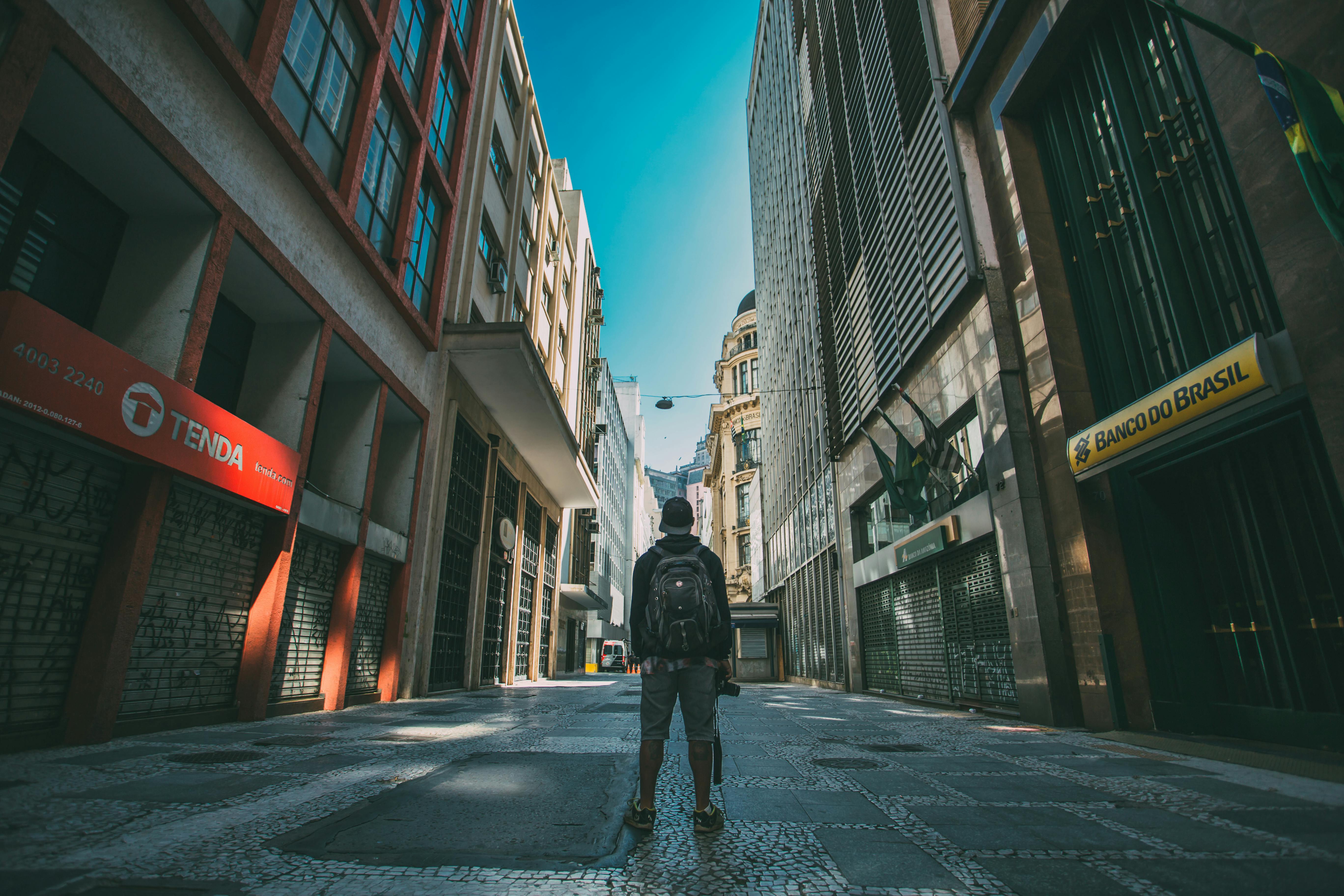 man standing on the road in between high rise buildings under blue sky