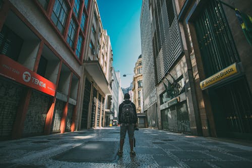 Man Standing on the Road in Between High-rise Buildings Under Blue Sky