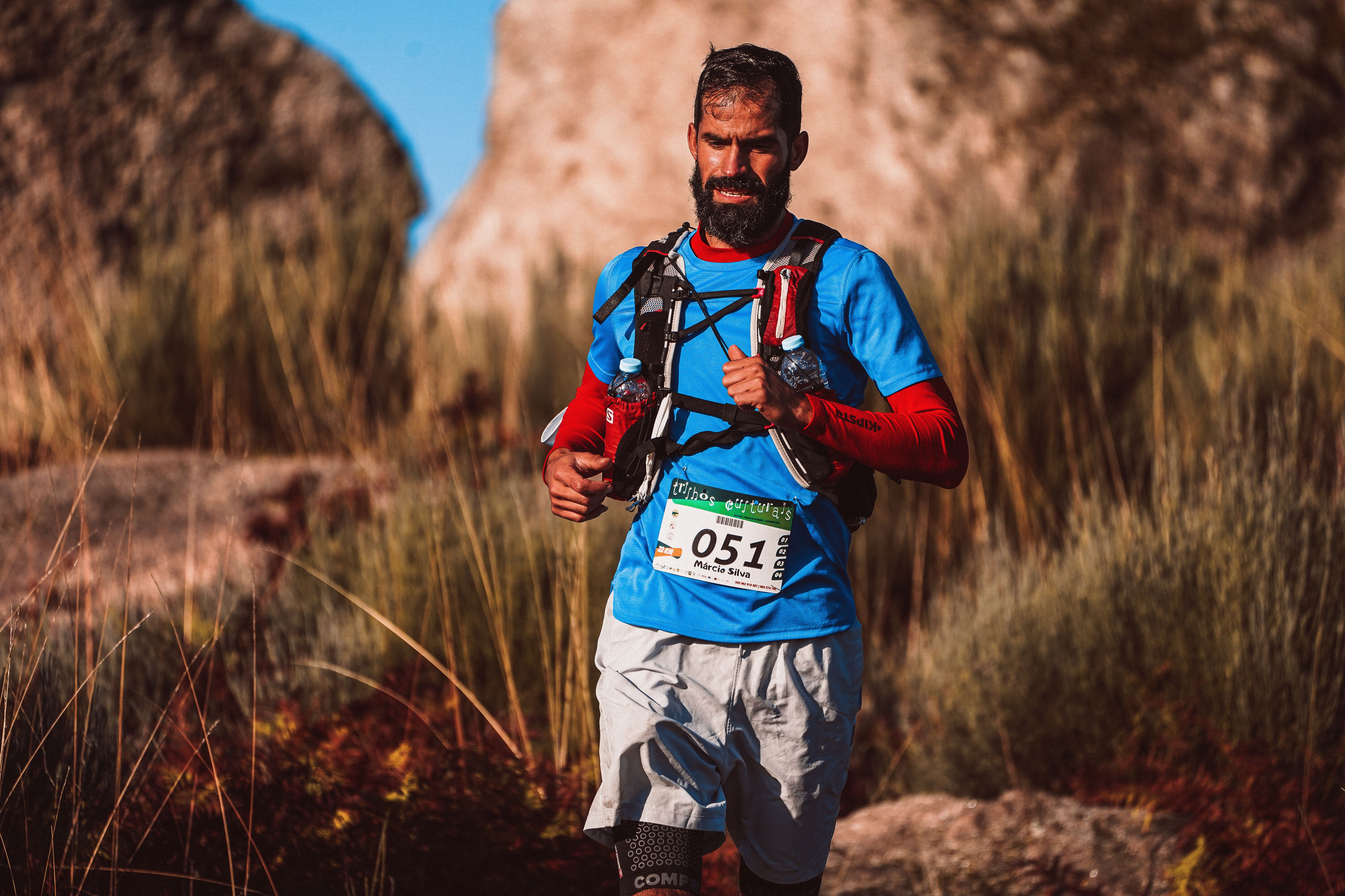 A bearded man participates in a trail running race through rugged outdoor terrain, showing determination.