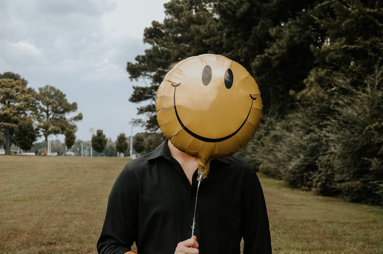 A Person Covering Face With Emoji Balloon