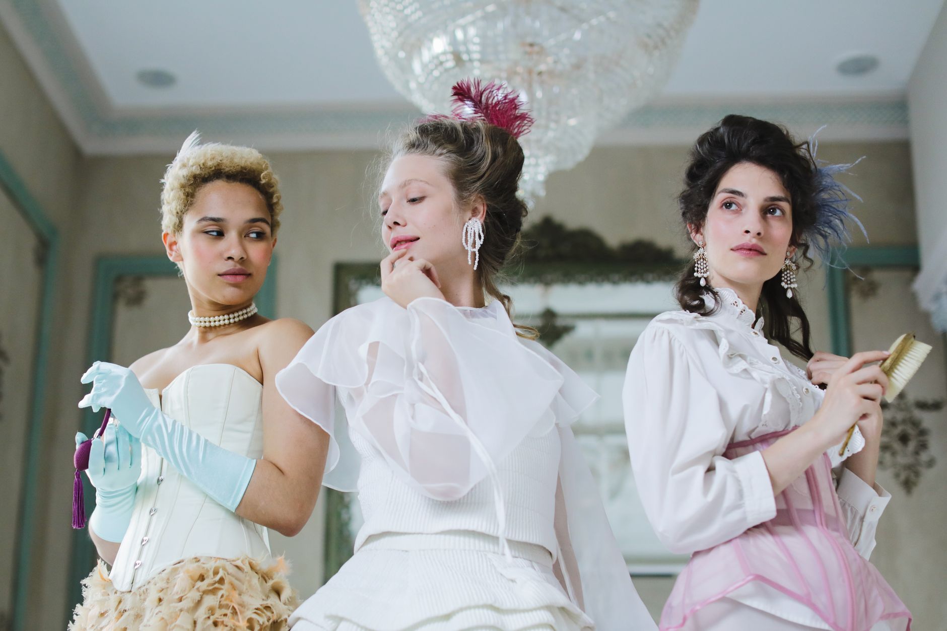 Elegant women posing in vintage attire with intricate hairstyles and accessories indoors.