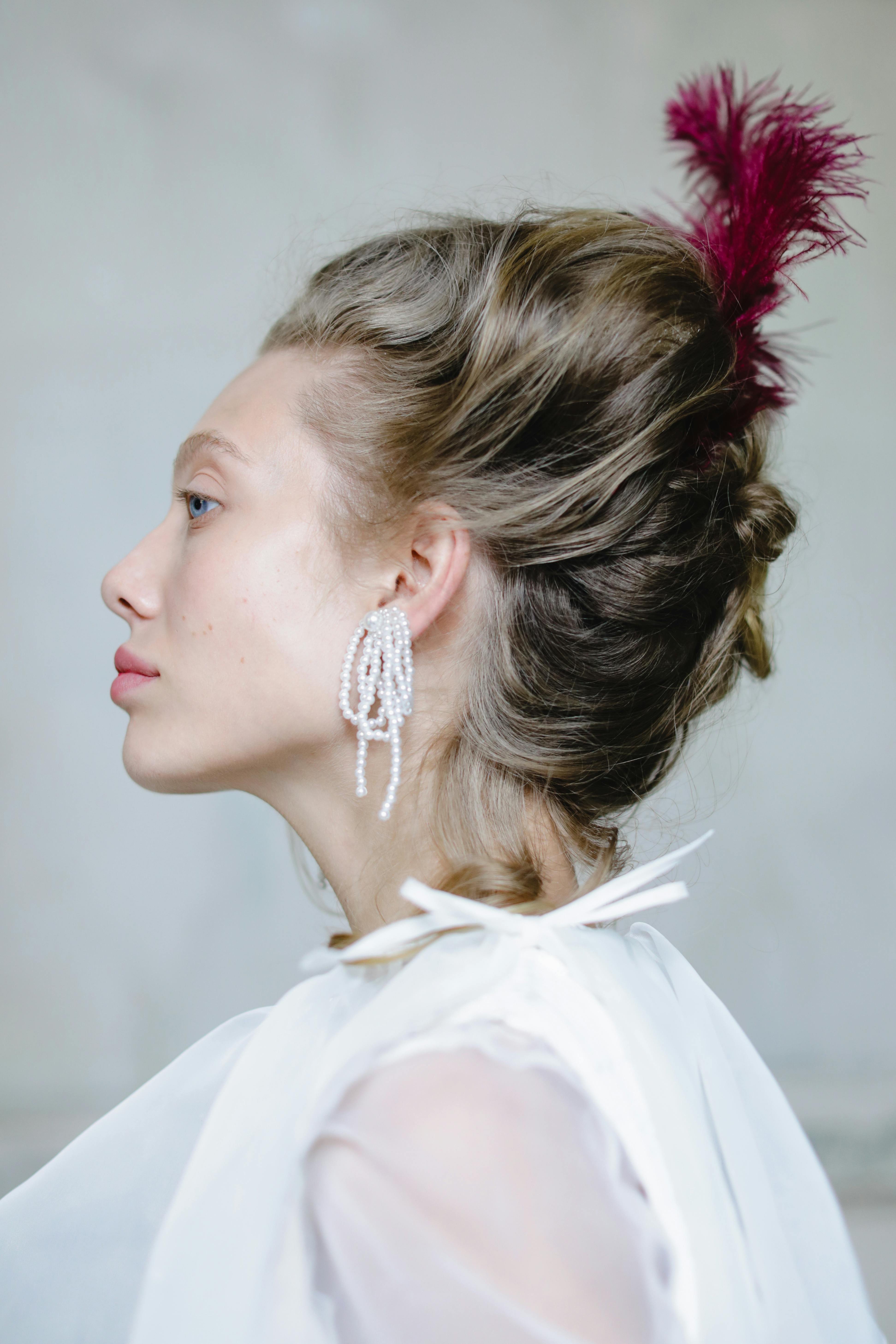 Side profile portrait of a young woman in period costume with elegant hairstyle and feather accessory.