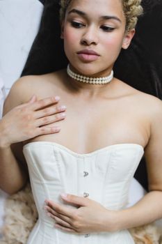 A young woman in a white corset lies gracefully, adorned with a pearl necklace.