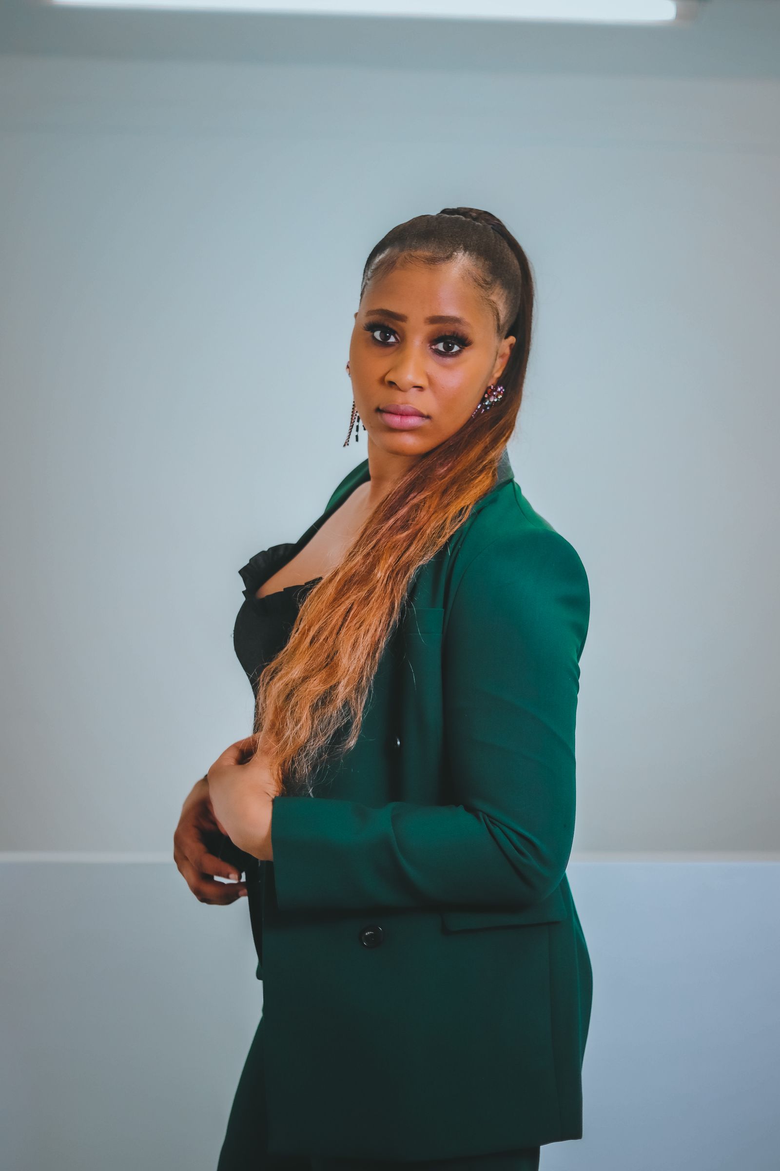 A woman in a dark green suit standing in front of a pale wall