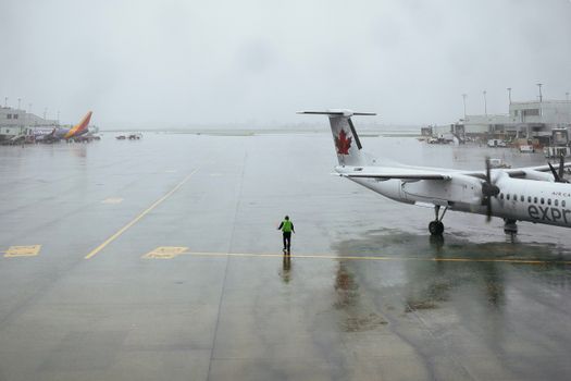 A lone worker on a rainy tarmac with planes at Portland Airport showcases the moody atmosphere.