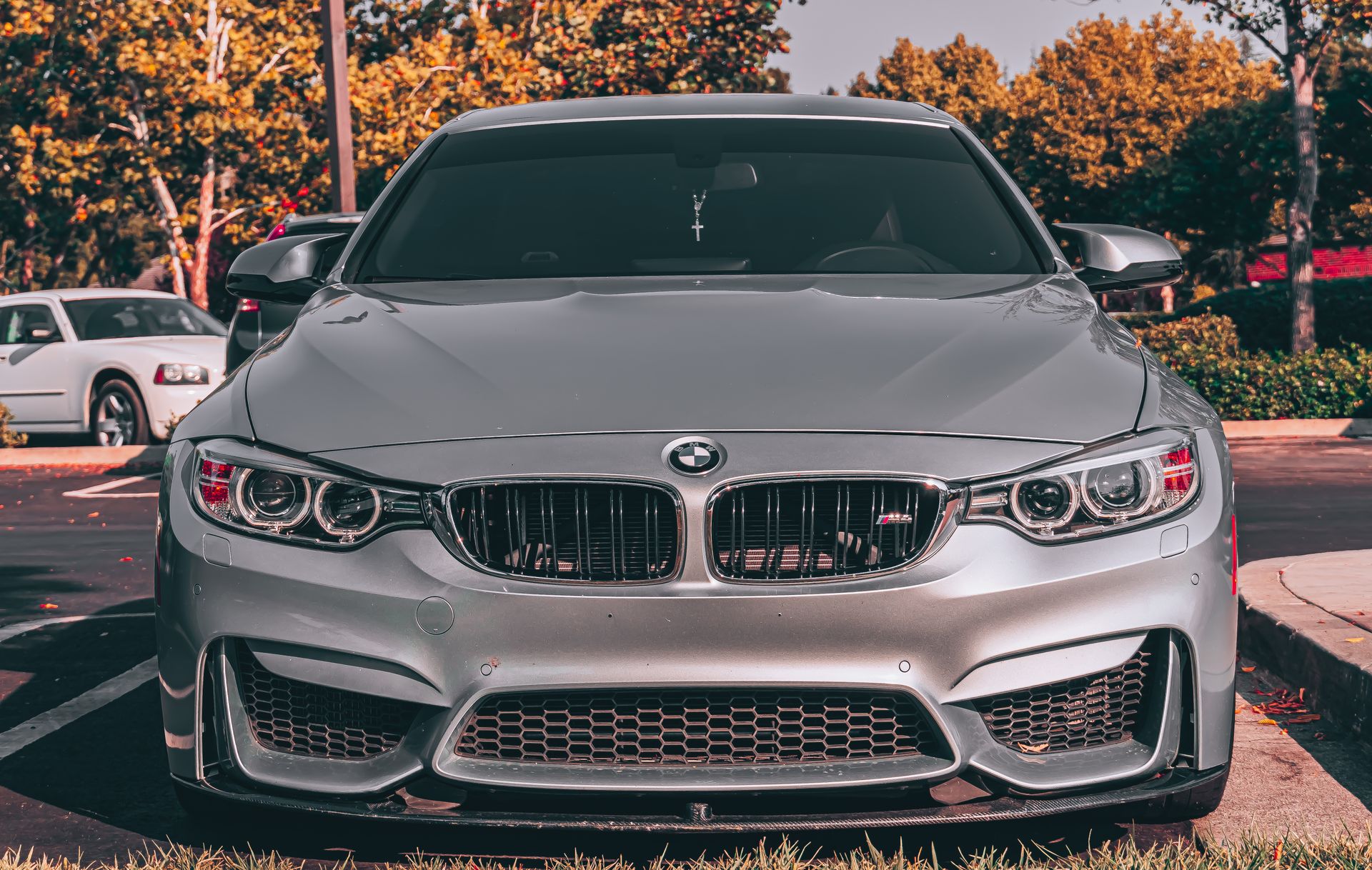 Close-up of a luxury silver BMW parked outdoors with autumn trees.