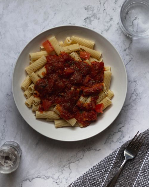 Free Top view of rigatoni pasta with tomato sauce, served on a marble table with utensils. Stock Photo