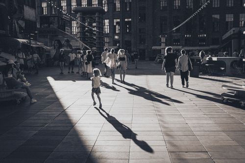 Free Black and white photo of people walking in a sunlit urban plaza casting shadows. Stock Photo