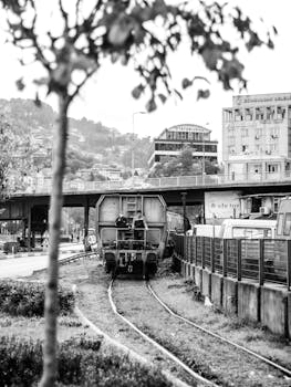 Monochrome image of a railway scene with an industrial urban backdrop.