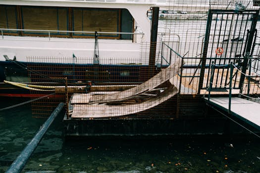 Photo by Mathias Reding A boat moored at a dockside in an industrial setting, featuring metal railings and ramps.