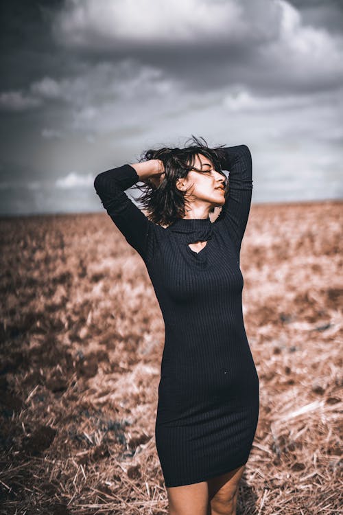 Woman in Black Long Sleeve Dress Standing on Brown Grass Field