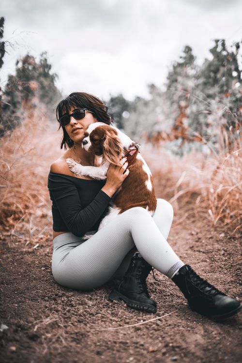 Free Woman sitting outdoors holding a brown and white dog, enjoying a serene moment in nature. Stock Photo