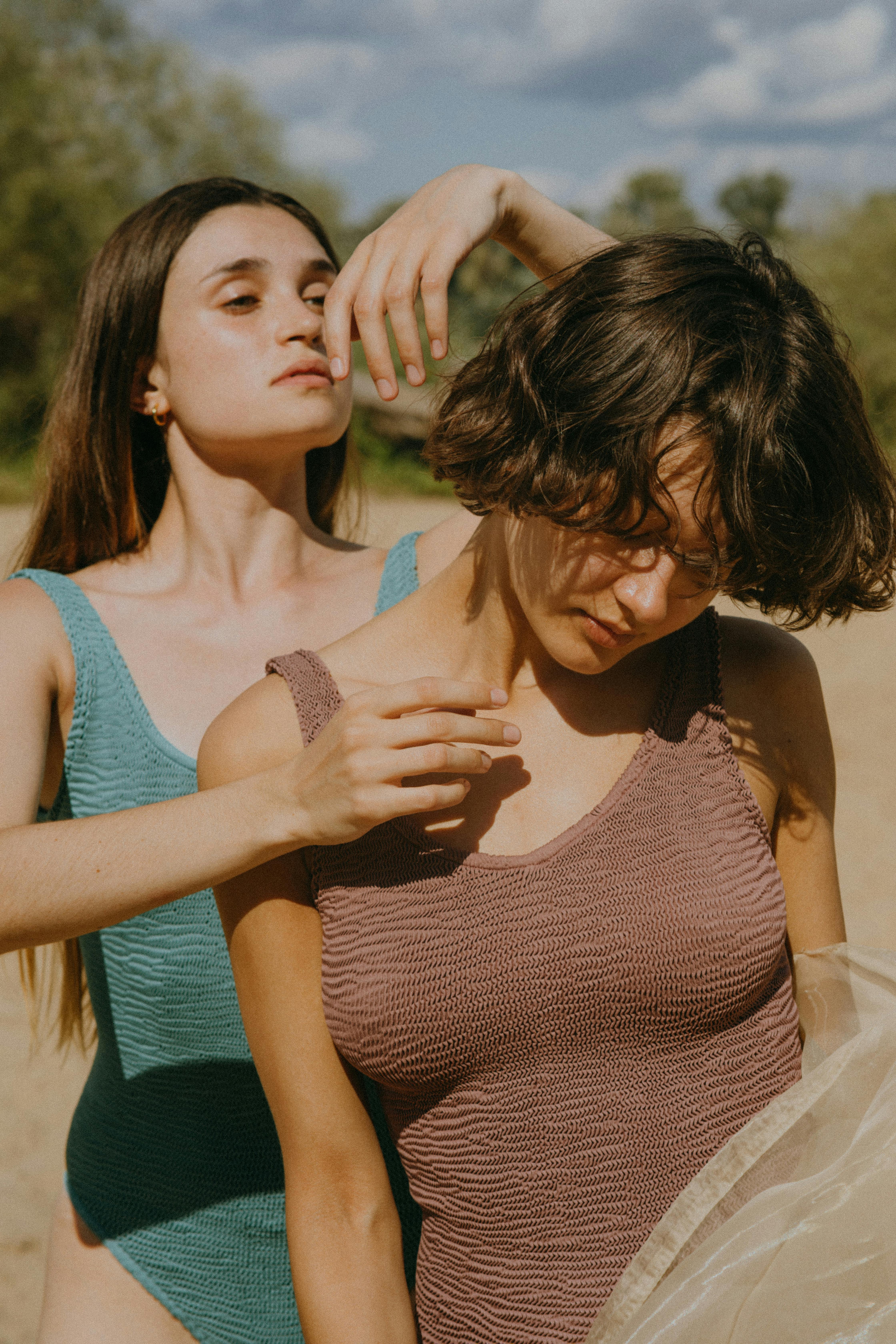 Two women in swimsuits pose artistically outdoors under the summer sun.