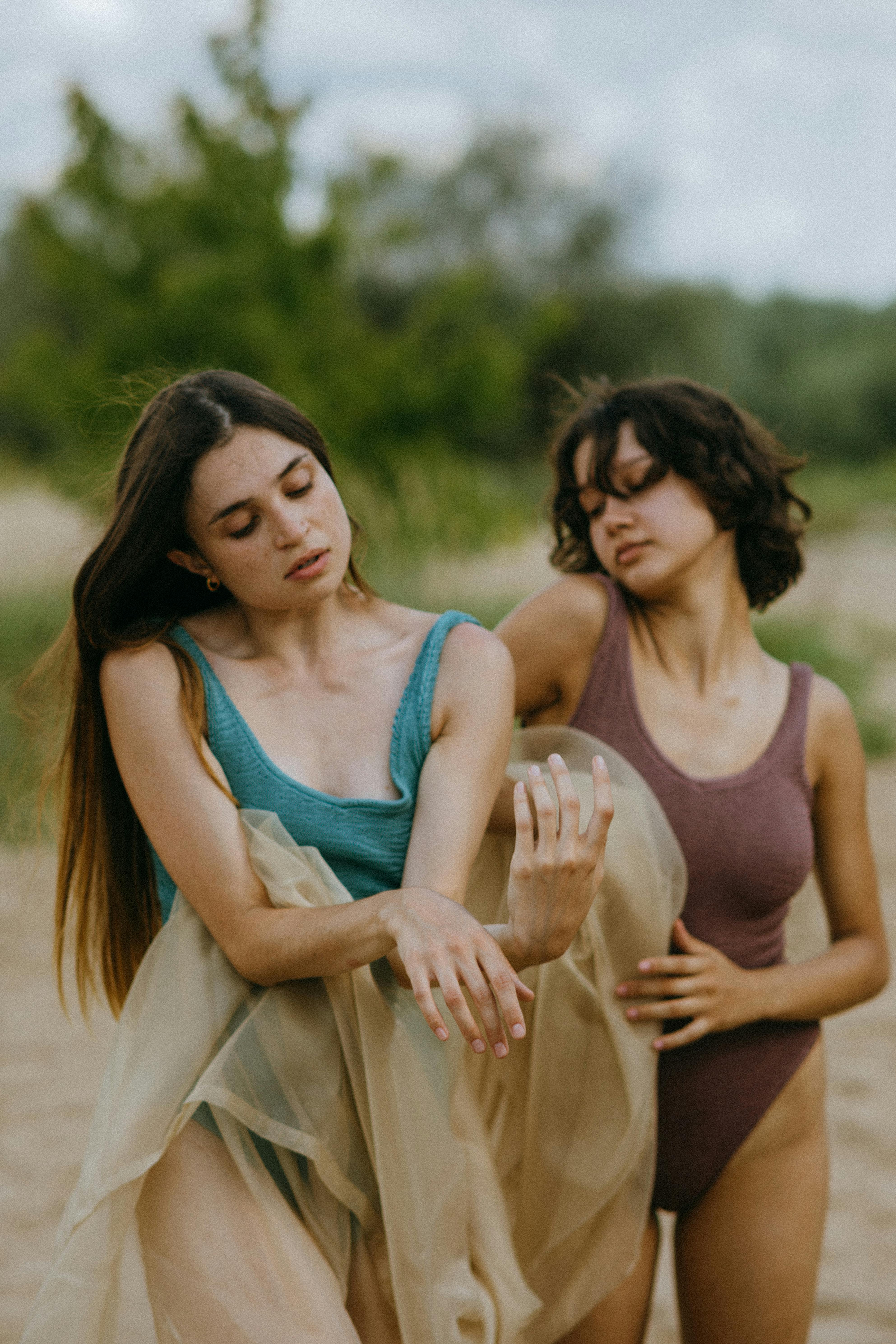 Two women posing gracefully on a sandy beach in summer attire, radiating elegance and leisure.