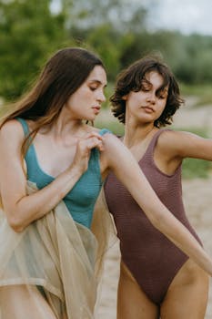 Two women in bodysuits perform a graceful dance outdoors surrounded by nature.