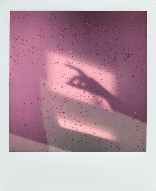 Creative shadow of hand gesture on a pink, glitter-specked wall, captured in artistic lighting.