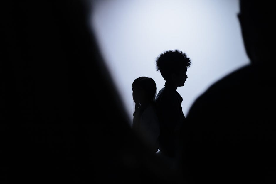 Silhouette of two children standing back to back in a studio shot with dramatic lighting.