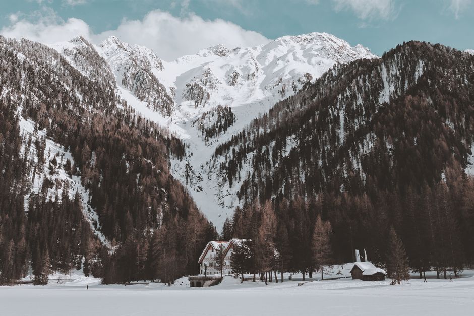 Scenic view of a snowy mountain peak with a cabin nestled among trees during winter.