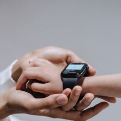 A parent holding a child's hand with a black smartwatch on the wrist