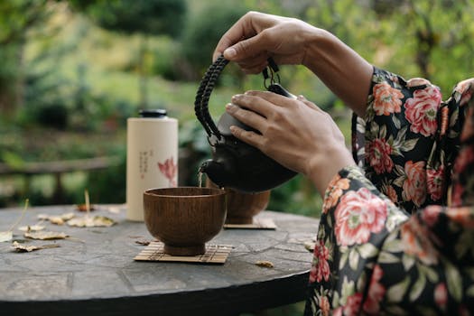 Hands pouring tea during a traditional Japanese tea ceremony in a peaceful garden setting.